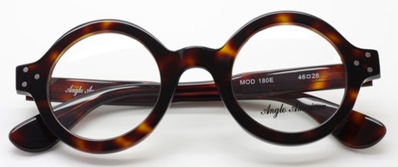 Puede incluir: Gafas redondas de carey con lentes transparentes. Las monturas tienen un sutil patr&oacute;n marr&oacute;n y negro. El nombre de la marca "Anglo American" est&aacute; impreso en la lente derecha y "MOD 180E" y "46D26" est&aacute;n impresos en la patilla derecha.