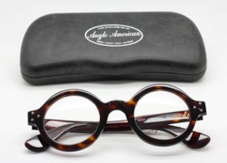 Puede incluir: Gafas redondas de montura de carey con lentes transparentes y una funda negra. La funda tiene las palabras "Anglo American" impresas.