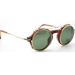 May include: Round sunglasses with a brown tortoiseshell frame and green lenses. The glasses have gold-colored metal accents on the bridge and temples. The arms are thin and gold-colored, with a curved ear piece.