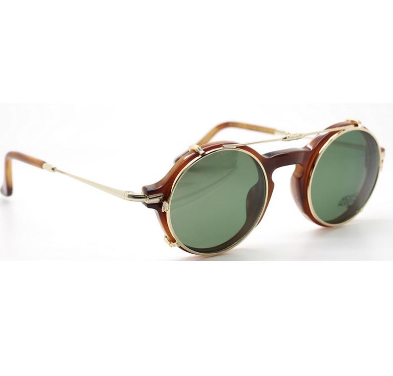 May include: Round sunglasses with a brown tortoiseshell frame and green lenses. The glasses have gold-colored metal accents on the bridge and temples. The arms are thin and gold-colored, with a curved ear piece.