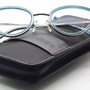 May include: A pair of silver and blue cat-eye glasses in a black leather case with the text "Archivio Moderno" embossed on the front.