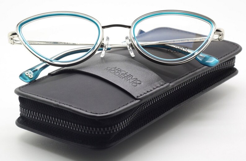 May include: A pair of silver and blue cat-eye glasses in a black leather case with the text "Archivio Moderno" embossed on the front.
