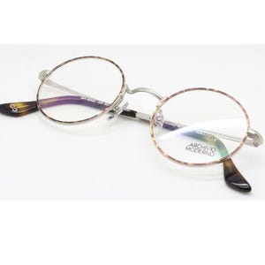 Puede incluir: Gafas redondas con montura plateada y detalles carey. Las lentes son transparentes y las patillas tienen un dise&ntilde;o marr&oacute;n oscuro y negro. La marca "ARCHIVIO MODERNO" es visible en la lente.