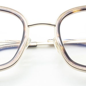 May include: Gold-rimmed eyeglasses with a tortoise shell frame. The lenses are clear and the arms are silver. The brand name "Archivio Moderno" is printed on the right arm.
