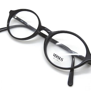 May include: Black round frame eyeglasses with clear lenses. The brand name "VERSUS" is printed on the right lens.