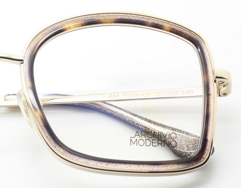 May include: Gold-rimmed eyeglasses with a tortoise shell pattern on the frame. The glasses have a clear lens and the text "AM 7009-02 53 18 140 ARCHIVIO MODERNO" is printed on the inside of the frame.