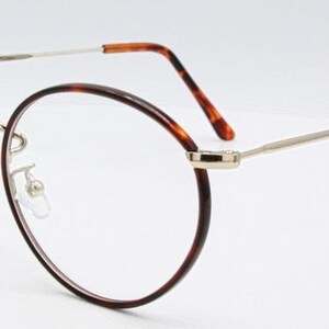 May include: Oval-shaped eyeglasses with a tortoiseshell pattern on the rims and temples. The frames are a combination of silver metal and brown tortoiseshell, with clear lenses. The glasses have a classic, vintage design.