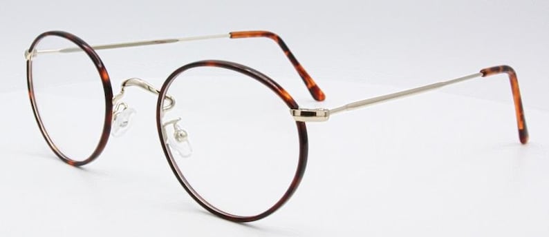 May include: Oval-shaped eyeglasses with a tortoiseshell pattern on the rims and temples. The frames are a combination of silver metal and brown tortoiseshell, with clear lenses. The glasses have a classic, vintage design.