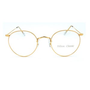 May include: Gold-rimmed eyeglasses with round lenses. The glasses have a thin, delicate frame and the text "Hilton Classic" is printed on the right lens. The overall design is minimalist and classic.