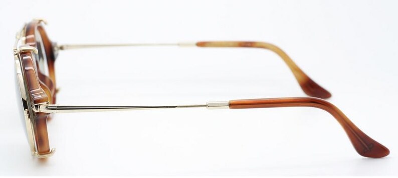 May include: Brown and gold-toned sunglasses with a tortoiseshell pattern on the frames. The arms are a combination of gold metal and brown plastic, with a curved design for a comfortable fit. The lenses are dark.