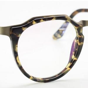 Puede incluir: Gafas con montura redonda y estampado carey. Las lentes son transparentes y el puente y las varillas met&aacute;licas tienen un acabado bronce. Las gafas tienen un dise&ntilde;o moderno y geom&eacute;trico.