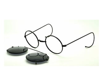 May include: Black round-framed glasses with clip-on sunglasses. The glasses have thin metal frames and the sunglasses are round and black.