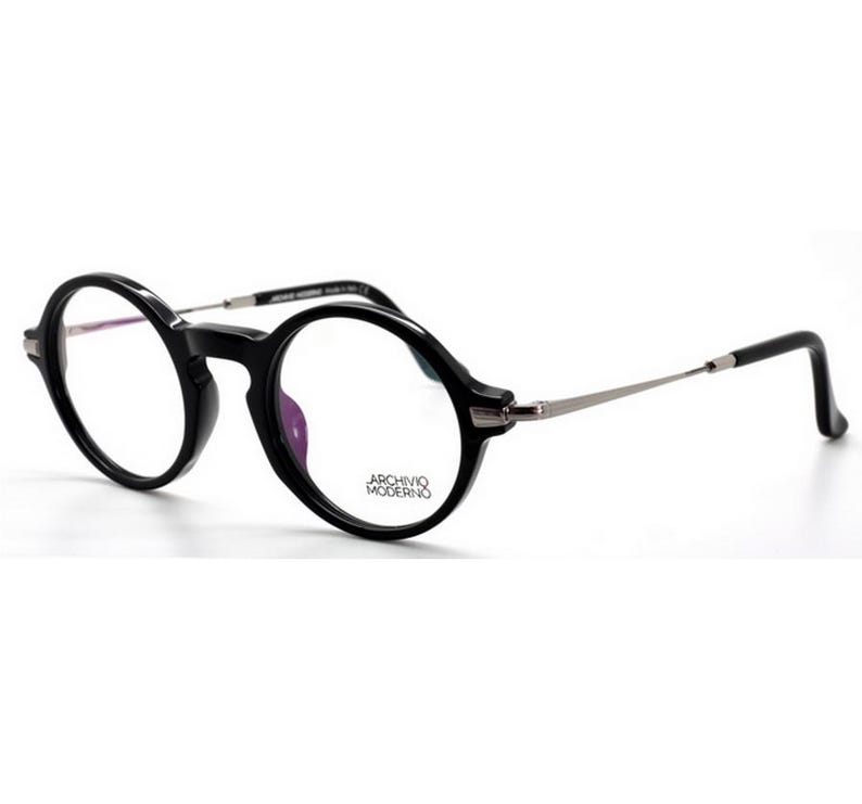 May include: Black round-frame eyeglasses with silver-toned temples. The glasses have a thick, glossy black frame and clear lenses. The brand name "ARCHIVIO MODERNO" is printed on the lower right lens.