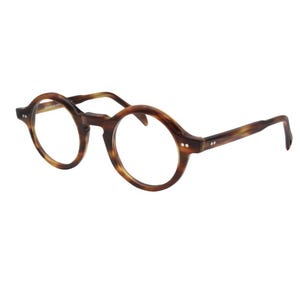 May include: Round tortoiseshell eyeglasses. The frames are brown with a speckled pattern, and the lenses are clear. The arms of the glasses are brown and curve slightly at the ends. The glasses are set against a white background.