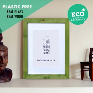 Puede incluir: Un marco de fotos de madera verde con un passe-partout blanco y un fondo blanco. El marco está hecho de madera real y tiene un frente de vidrio real. El marco está hecho a mano en el Reino Unido y está libre de plástico. El marco está sentado en un estante blanco con una estatua de madera y una pequeña silla de madera.