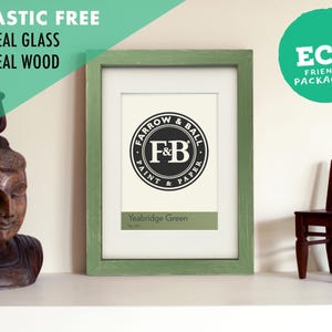 Könnte beinhalten: Ein rechteckiger Bilderrahmen mit einem abgenutzten, salbeigrünen Holzrahmen, einem weißen Passepartout und einem Druck mit dem schwarz-weißen Farrow & Ball Paint & Paper Logo sowie dem Text Yeabridge Green No. 287 unten.