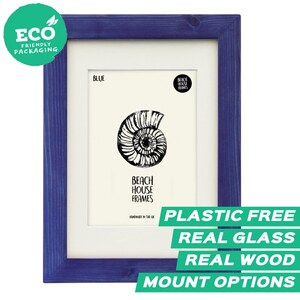 May include: A rectangular blue wooden picture frame with a white mount. The centre features a black and white illustration of an ammonite fossil. Text on the print includes "BLUE", "BEACH HOUSE FRAMES", and "HANDMADE IN THE UK".