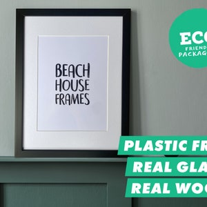 Könnte beinhalten: Ein gerahmter Druck mit dem Text "BEACH HOUSE FRAMES" in einem schwarzen Rahmen. Das Bild enthält auch einen grünen Kreis mit den Worten "ECO FRIENDLY PACKAGING". Darunter stehen die Worte "PLASTIC FREE, REAL GLASS, REAL WOOD".