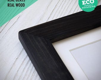 Puede incluir: Un marco de fotos de madera negra con una esquina en inglete y un paspartú blanco. El marco presenta una textura de veta de madera visible. El texto en la imagen dice: PLASTIC FREE, REAL GLASS, REAL WOOD, y un sello verde: ECO FRIENDLY PACKAGING.