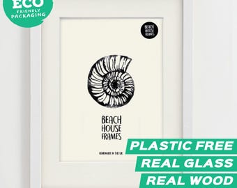 Könnte beinhalten: Ein weißer rechteckiger Rahmen mit einem cremefarbenen Druck einer schwarzen Ammoniten-Fossil-Illustration. Der Druck zeigt den Text "BEACH HOUSE FRAMES" und "HANDMADE IN THE UK" unter dem Fossil sowie ein kreisförmiges Logo.