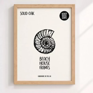 The image is a framed artwork featuring a black and white illustration of a spiral shell or nautilus shell. The text on the frame reads "SOLID OAK" and "BEACH HOUSE FRAMES" along with "HANDMADE IN THE UK".