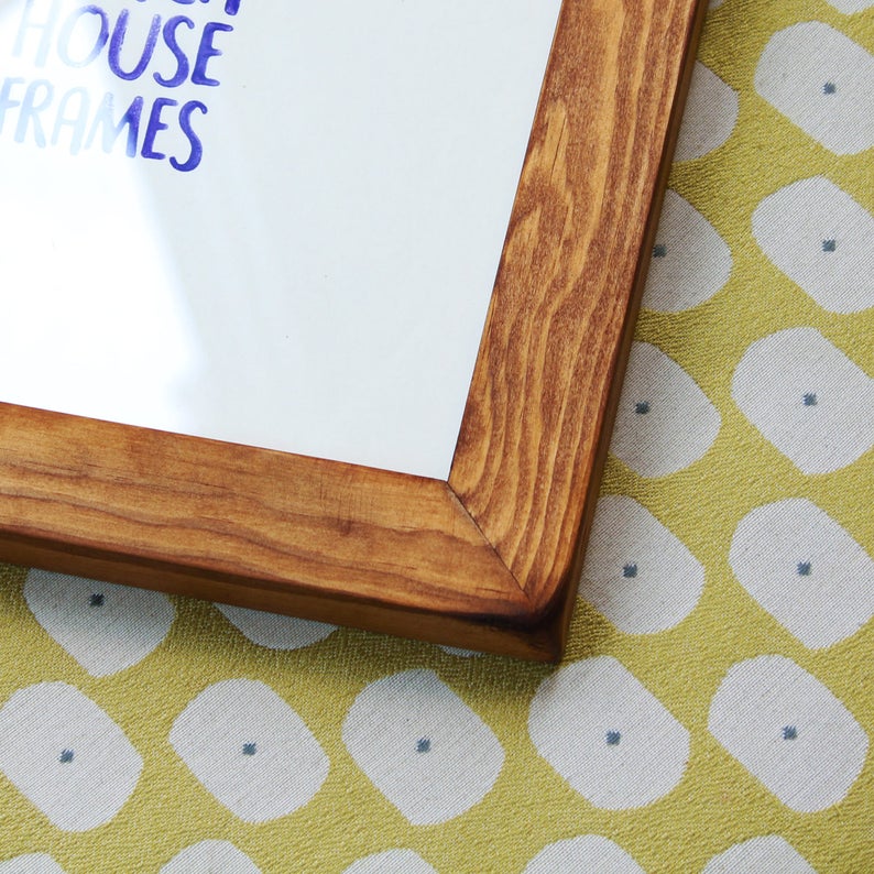May include: A close-up of the corner of a wooden picture frame with a natural wood finish. The frame is sitting on a yellow and white patterned fabric.