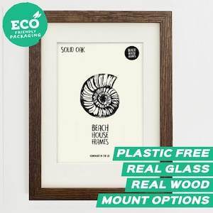 May include: A dark brown solid oak picture frame containing a white print with a black ink illustration of an ammonite fossil. The text on the print reads SOLID OAK, BEACH HOUSE FRAMES, and HANDMADE IN THE UK. The frame features a white mat board.