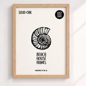 The image is a framed artwork featuring a black and white illustration of a spiral shell or nautilus shell. The text on the frame reads "SOLID OAK" and "BEACH HOUSE FRAMES" along with "HANDMADE IN THE UK".