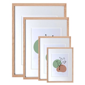May include: Four wooden picture frames of different sizes, all with a natural wood finish. The frames are nested inside each other, with the smallest frame in the center and the largest frame on the outside. The frames are all empty, but the smallest frame has a white mat and a simple abstract design printed on the paper inside.
