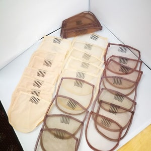 Peut inclure: Une collection de bonnets de perruque beiges et bruns avec des peignes. Les bonnets sont faits d'un matériau en maille fine et ont plusieurs rangées de peignes le long des bords.