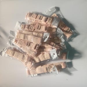 Puede incluir: Una colección de múltiples extensores de sujetador de color beige, cada uno empaquetado individualmente en fundas de plástico transparente. Estos extensores de tela cuentan con cierres de corchetes metálicos para ajustar la talla.