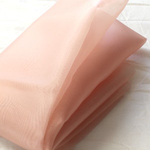 May include: A folded piece of peach-colored sheer fabric. The fabric is translucent and has a soft, delicate texture.