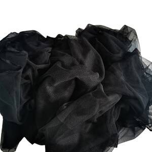Pode incluir: Tecido de tule preto com uma textura macia e delicada. O tecido está amassado e reunido, mostrando sua qualidade arejada e leve.