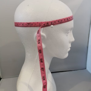 Puede incluir: Una cabeza de poliestireno blanco con una cinta métrica rosa envuelta alrededor. La cinta indica 55, 56, 3, 4, 5, 6, 7, 8, 9, 10, 25, 26, 27, 28, 29, 30, 31.