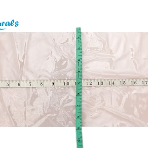 Peut inclure: Une feuille de matière blanche translucide est mesurée avec un mètre ruban. La feuille mesure 56 cm de large et 38 cm de long.