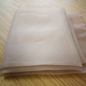 May include: A folded piece of sheer, light brown fabric. The fabric is smooth and has a subtle sheen.