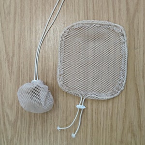 May include: Two beige mesh laundry bags with white drawstrings. One bag is round, and the other is rectangular. The bags are made of a fine mesh material and are designed to protect delicate items during washing.