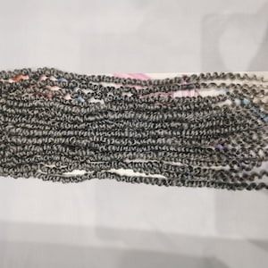 May include: A pack of gray curly synthetic hair extensions. The hair is in a loose, wavy style and is ready to be used for braiding or other hair styling techniques.