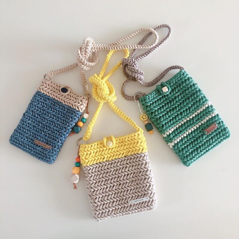 May include: Three crocheted phone pouches in blue, green, and beige with yellow accents. The pouches have a herringbone pattern and are attached to a long strap.