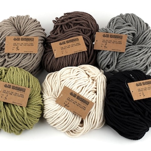 Op de afbeelding: Zes spoelen natuurlijke katoenen touw in verschillende kleuren, waaronder beige, bruin, grijs, groen en zwart. Elke spoel heeft een bruin papieren etiket met Koreaanse tekst.