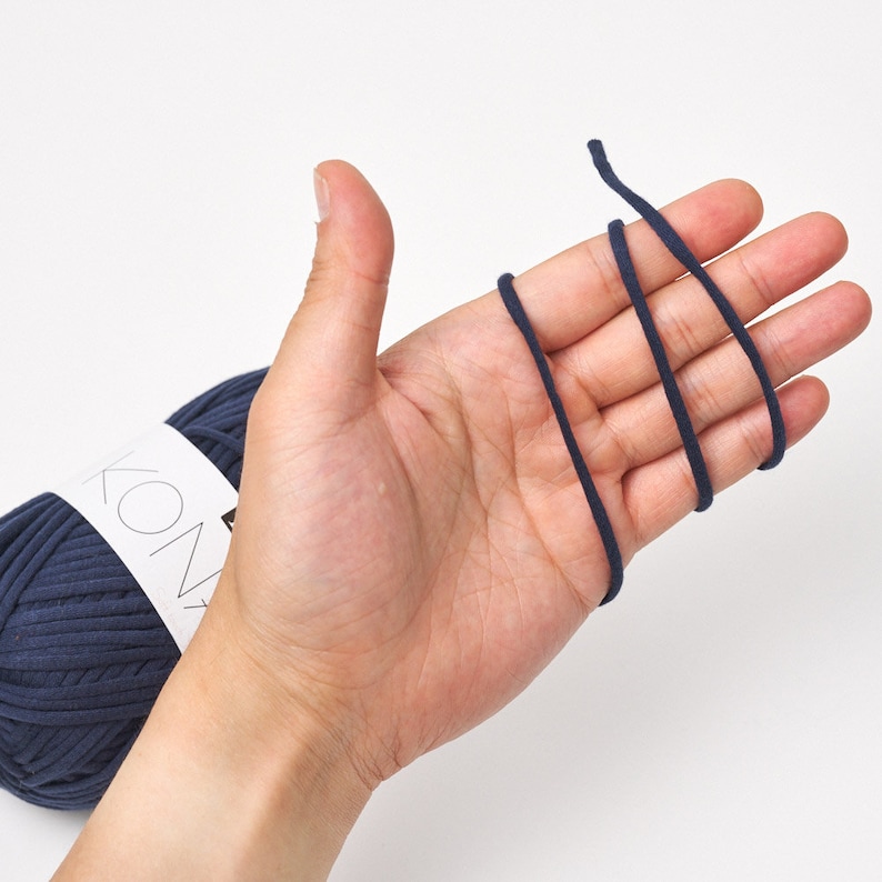 May include: A ball of dark blue yarn with the word "KONA" printed on the label. A length of the yarn is wrapped around a hand.