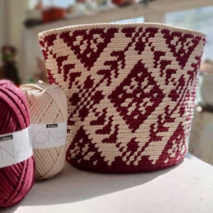 May include: Two balls of yarn, one burgundy and one beige, with the label "Lina Kona" on each. A crocheted basket with a geometric pattern in burgundy and beige.