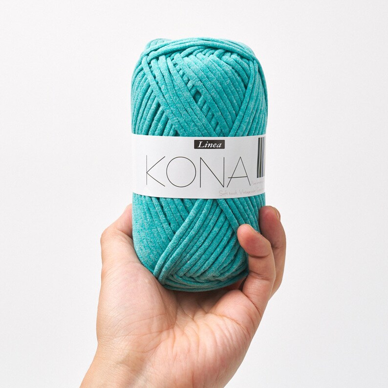 May include: A teal blue ball of yarn labeled "Kona" with the word "Linea" above it.