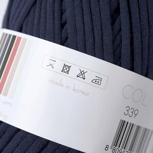 May include: A close-up of a dark blue yarn ball with a white label. The label has care instructions, "made in Korea", and a color code of "COL 339".