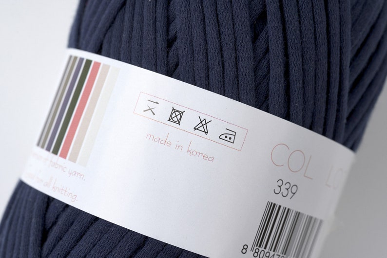 May include: A close-up of a dark blue yarn ball with a white label. The label has care instructions, "made in Korea", and a color code of "COL 339".