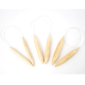 May include: Set of five wooden knitting needles with cords. The needles are beige and have a smooth finish. The cords are white and are attached to the needles. The needles are labeled with their sizes in millimeters: 3.5 mm, 3.75 mm, 4.0 mm, 4.5 mm, and 5.0 mm.