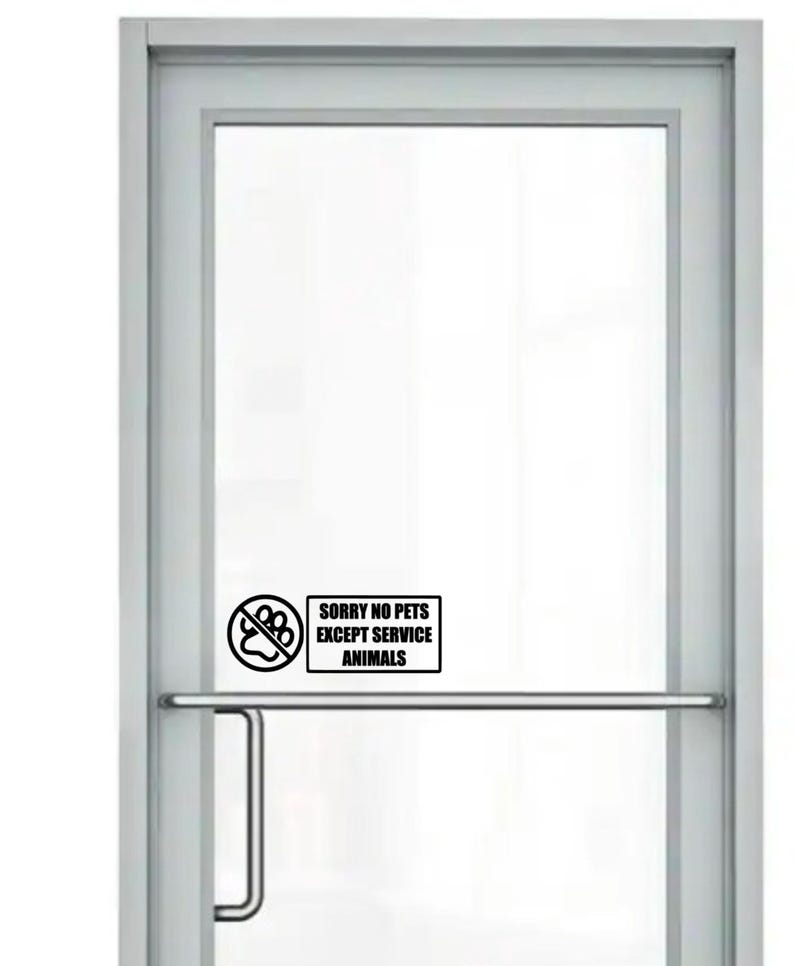 Op de afbeelding: Een glazen deur met een zilveren frame en een horizontale stanggreep. Een zwart-wit bord op de deur met de tekst "SORRY NO PETS EXCEPT SERVICE ANIMALS" met een doorgestreept pootafdruk-symbool.