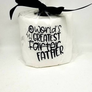 May include: A white gift wrapped in clear cellophane and tied with a black ribbon. The gift has the text "#1 World's Greatest Father" in black lettering.