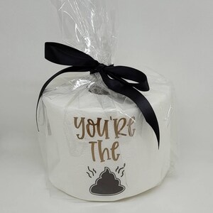 May include: A roll of white toilet paper wrapped in clear cellophane and tied with a black ribbon. The roll has the words "you're the" and a graphic of a pile of poop.