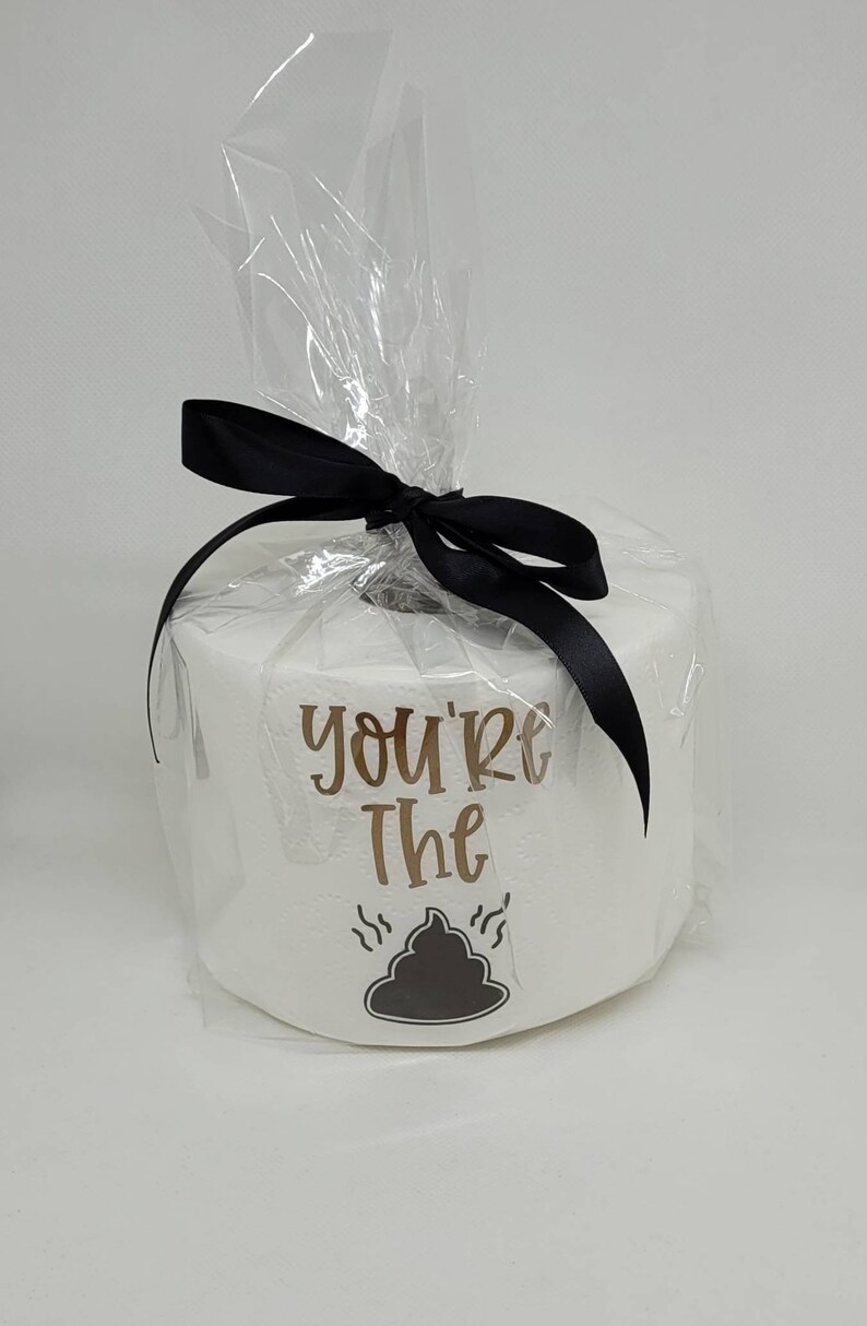 May include: A roll of white toilet paper wrapped in clear cellophane and tied with a black ribbon. The roll has the words "you're the" and a graphic of a pile of poop.